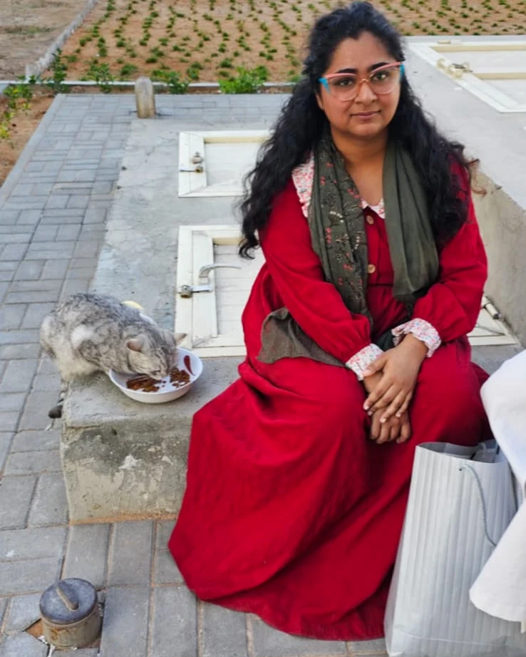 Aysha seated quietly, a cat eating beside her